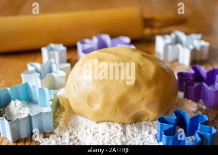 Eine Kugel von Zucker Plätzchenteig in einem Bett von Mehl. Rolling Pin unscharf im Hintergrund. Verschiedene Blumen- und Schneeflocke Ausstecher rund um Ball von Teig Stockfoto