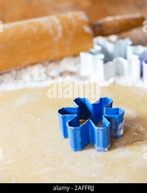 Eine blaue Blume Cookie Cutter Ein ausgerollt Zucker Plätzchenteig. Zusätzliche Ausstechformen und Nudelholz unscharf im Hintergrund. Holz- Oberfläche. Stockfoto