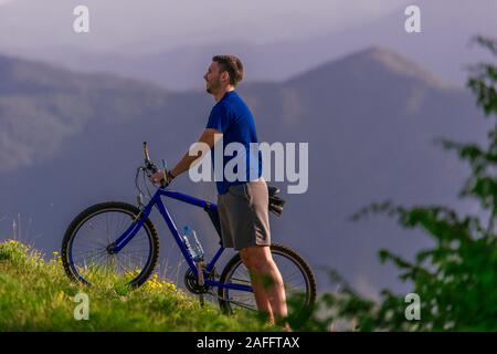 Müde Radfahrer wischte seine Schweiß aus seinem Gesicht, während sein Fahrrad bergauf schieben ein Feldweg in einem Berg. Stockfoto