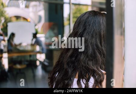 Junge Frau mit lockigem Haar sitzt in Kaffee Restaurant im Freien Stockfoto