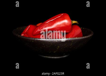 Menge ganze eingelegte rote Paprika in glasierte Schüssel auf schwarzem Glas isoliert Stockfoto