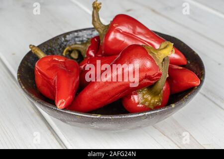 Menge ganze eingelegte rote Paprika in glasierte Schüssel auf weißem Holz Stockfoto