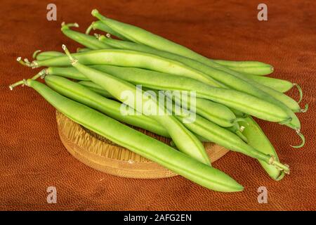 Menge ganze Snap grüne Bohne auf runden Bambus Untersetzer auf cognac Leder Stockfoto