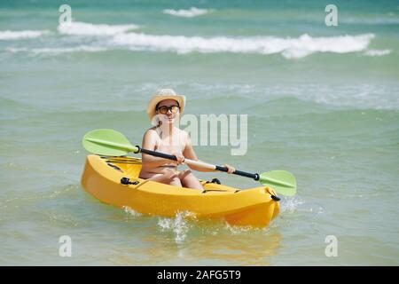 Glücklich lächelnde junge hübsche Asiatin im Stroh Hut Kajakfahren im Meer im Sommer Tag Stockfoto