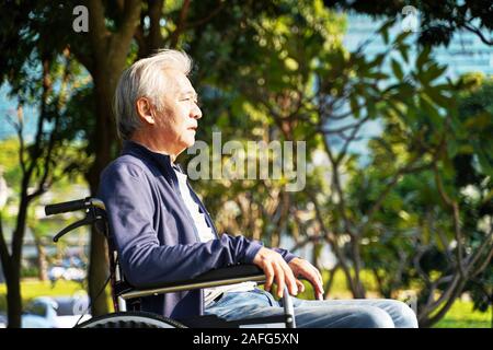 Seitenansicht des asiatischen älterer Mann sitzt im Rollstuhl im Freien Stockfoto