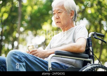 Traurig asiatischen älterer Mann sitzt draußen im Rollstuhl Stockfoto