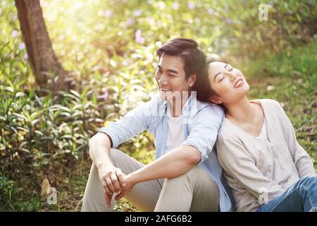 Glückliche junge asiatische Paare sitzen auf dem Boden sprechen Tagträumen Stockfoto