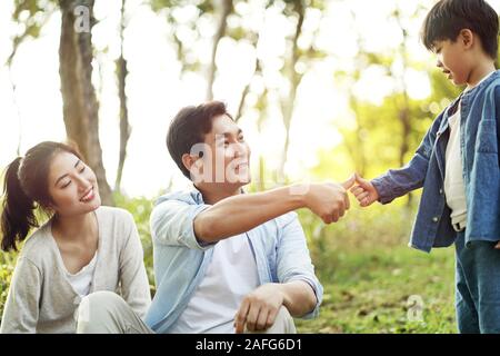 Asiatische Vater und Sohn Versiegelung ist ein Abkommen, das durch Drücken der Daumen zusammen draußen im Park Stockfoto