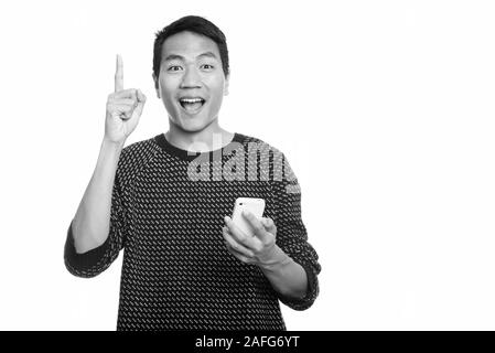 Studio shot junger asiatischer Mann glücklich lächelnd, während sie Handy und zeigen mit dem Finger auf Stockfoto