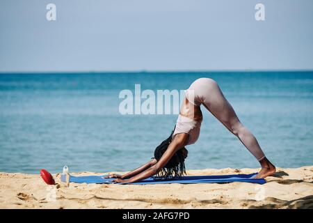 Junge passende Frau tun in den nach unten schauenden Hund Übung zwischen Asanas beim Üben Yoga am Strand Stockfoto