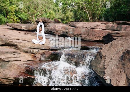 Schöne junge Frau sitzen, Wasserfall und genießen die Meditation in der Natur Stockfoto