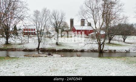 Luftaufnahme von traditionellen Farm in Pennsylvania, rotes Gebäude und Scheune, einem kleinen Fluss im Vordergrund, winterlandscape im Schnee Stockfoto