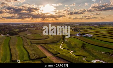 Magischen Sonnenuntergang in ländlichen amerikanischen Landschaft, Luftaufnahme von Mais Felder, Wiesen und Weiden, Farmen und einer kleinen, gewundenen Bach, Sonnenstrahlen durch die Wolken Stockfoto