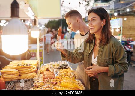 Glückliche junge Frau kaufen Schweinefleisch vom Grill Spieß mit traditionellen vietnamesischen Street Food stall Stockfoto