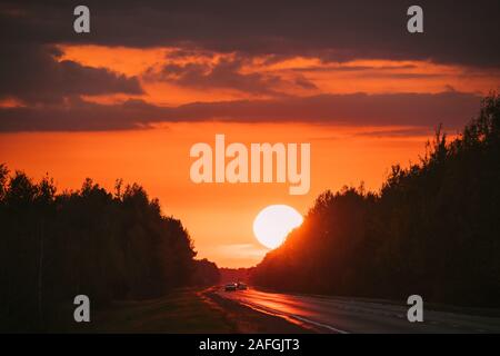 Autos in Bewegung auf der Straße, Autobahn. Asphalt Autobahn Autobahn gegen den Hintergrund der grossen Sonnenuntergang Sun Travel Reise Konzept. Sonne über der Straße. Stockfoto