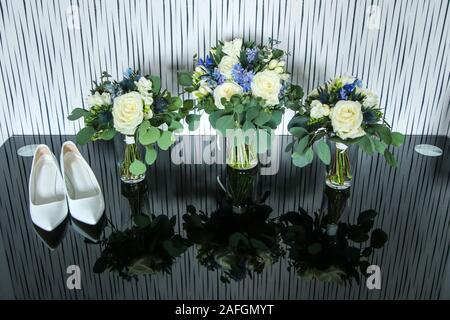Das Bild von der Ausrüstung für die Braut für die Hochzeit. Die Blumensträuße Rosen stehen auf dem Tisch mit den Schuhen. Stockfoto