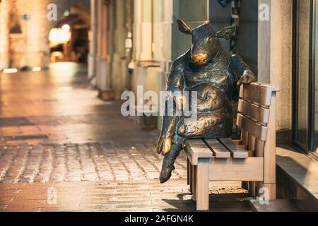 Tallinn, Estland - 5. Dezember 2016: Black Angus Skulptur - Bronze Stier Kuh Statue, sitzt auf der Bank in der Nähe von Cafe. Nacht ansehen. Stockfoto