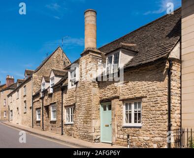 Eine Reihe sonnenbeleuchteter, denkmalgeschützter kleiner Steinhäuser, eines mit einem großen kreisförmigen Steinkamin, St. George's Street, Stamford, Lincolnshire, England, Großbritannien Stockfoto