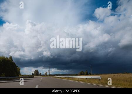 Dramatische Landschaft von der Mitte der Straße in das Ende des Sommers genommen. Schwere schönen stürmischen Wolken schließen, wenn Sonne scheint. Stockfoto