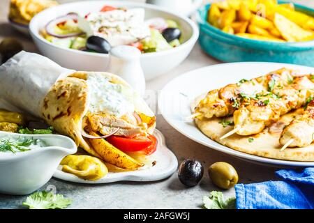 Griechisches Essen: Salat, Hähnchen Souvlaki, Gyros und gebackene Kartoffeln auf einem grauen Hintergrund. Traditionelle griechische Küche Konzept. Stockfoto