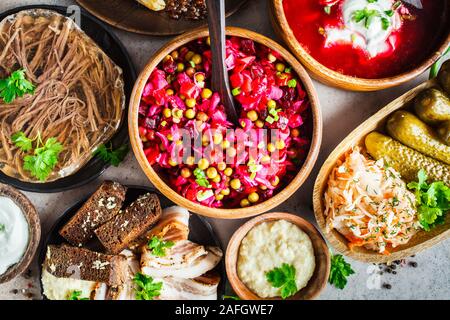 Traditionelle russische Küche Konzept. Borsch, sülze Fleisch, Speck, Pfannkuchen, Salat Vinaigrette und Sauerkraut, grauen Hintergrund. Stockfoto