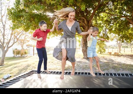 Mutter spielt mit Kindern auf Outdoor Trampolin im Garten Stockfoto