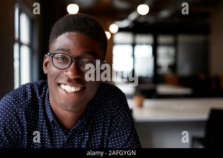 Tausendjährige männlichen Schwarzen kreative Sitzen an einem Schreibtisch in einem Büro lächelnd in die Kamera, in der Nähe Stockfoto