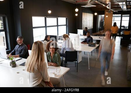 Ansicht des kreativen Kollegen arbeiten bei Schreibtische und gehen durch einen geschäftigen Büro Stockfoto