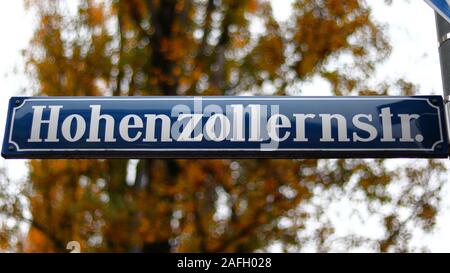 Nahaufnahme eines Straßennamens mit gelben Bäumen auf verschwommenem Hintergrund in München Stockfoto