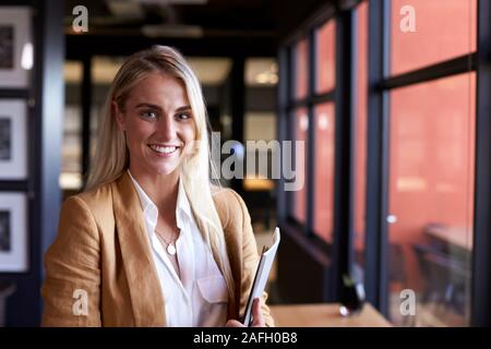 Tausendjährige weiss blond Geschäftsfrau lächelnd in die Kamera durch das Fenster im Büro, in der Nähe Stockfoto