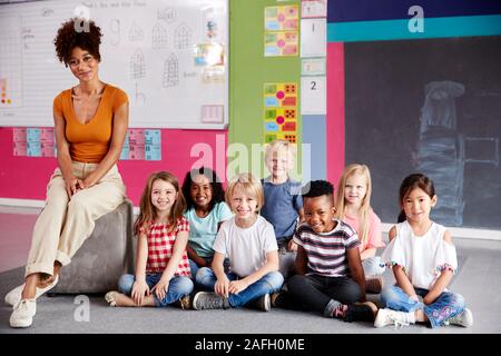 Portrait von Grundschülern sitzen auf dem Boden im Klassenzimmer mit Lehrerin Stockfoto