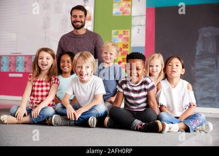 Portrait von Grundschülern sitzen auf dem Boden im Klassenzimmer mit männlichen Lehrer Stockfoto