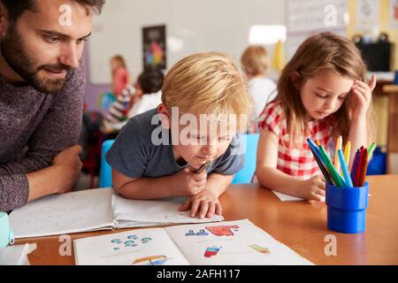 Grundschule Lehrer helfen Schülerinnen und Schüler bei der Arbeit am Schreibtisch im Klassenzimmer Stockfoto