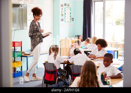 Lehrerin mit digitalen Tablet lehrt Gruppe von Uniformierten Grundschule Schülerinnen und Schüler In der Schule Klassenzimmer Stockfoto