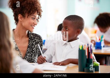 Frau Grundschullehrer, die männlichen Schüler tragen Uniform Eins zu Eins Unterstützung im Klassenzimmer Stockfoto