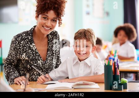 Portrait von Frau Grundschullehrer, die männlichen Schüler tragen Uniform Eins-zu-Eins-Unterstützung Stockfoto