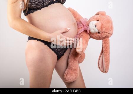 Close-up schwangeren Bauch mit Hase Spielzeug. Schöne schwangere Frau. Schwangerschaft, Elternschaft, Vorbereitung und Erwartung Konzept. Stockfoto