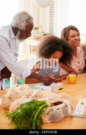 Großeltern am Tisch sitzen bei den Hausaufgaben helfen, Enkelin Stockfoto