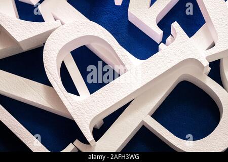 Weiße Buchstaben ausschneiden aus Schaumstoff ohne Lackierung auf einem blauen Hintergrund. Leer, für die Dekoration, Logo, Stockfoto