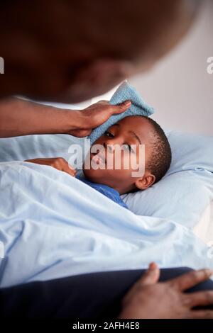 Vater die Sorge für die Kranken Sohn krank im Bett mit Temperatur Stockfoto