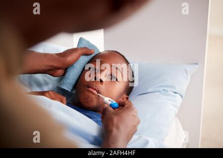 Vater die Sorge für die Kranken Sohn krank im Bett, die Temperatur mit dem Thermometer Stockfoto