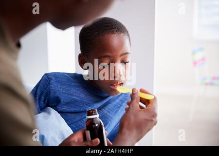 Vater kranken Sohn krank im Bett Medizin aus der Flasche Stockfoto