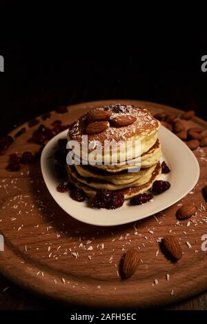 Vertikale Aufnahme des Stapels der Pfannkuchen mit den Mandeln und Rosinen mit Kokospulver bedeckt Stockfoto