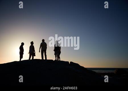 Silhouette der älteren Freunde stehen auf Felsen auf dem Seeweg durch Vermietungen bei Sonnenuntergang Stockfoto