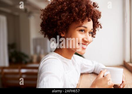 Junge Frau Entspannen im Loft Apartment Blick Aus Fenster mit heißen Getränken Stockfoto