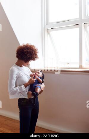 Liebevolle Mutter halten Schlafen Neugeborene durch Fenster in Loft Apartment
