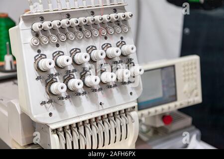 Industrielle weiße Nähmaschine für Stickerei macht schwarzem Logo mit dem Buchstaben S mit schwarzen Faden auf einem roten Hintergrund aus perforiertem Leder Stockfoto