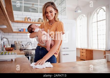 Multi-Tasking Mutter hält Schlafendes Baby Sohn und reinigt in Küche Stockfoto