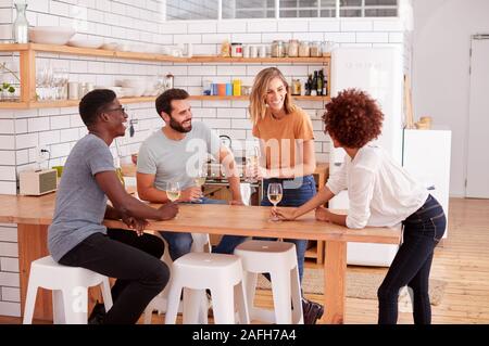 Zwei Paare, die Entspannung in der Küche zu Hause bei einem Glas Wein zusammen gesprochen Stockfoto