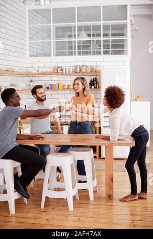 Zwei Paare, die Entspannung in der Küche zu Hause einen Toast mit einem Glas Wein zusammen Stockfoto